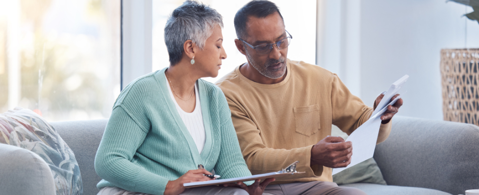 An African American couple sitting on a couch reviewing health insurance information and physician bills